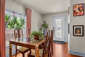 Ein Essbereich mit einem Glastisch, Holzstühlen, einem Blumentopf und Blick auf Bäume durch große Fenster.
