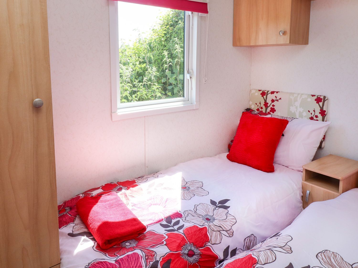 A bedroom with a single bed, a nightstand, a wooden cabinet, and a window with a view of greenery.