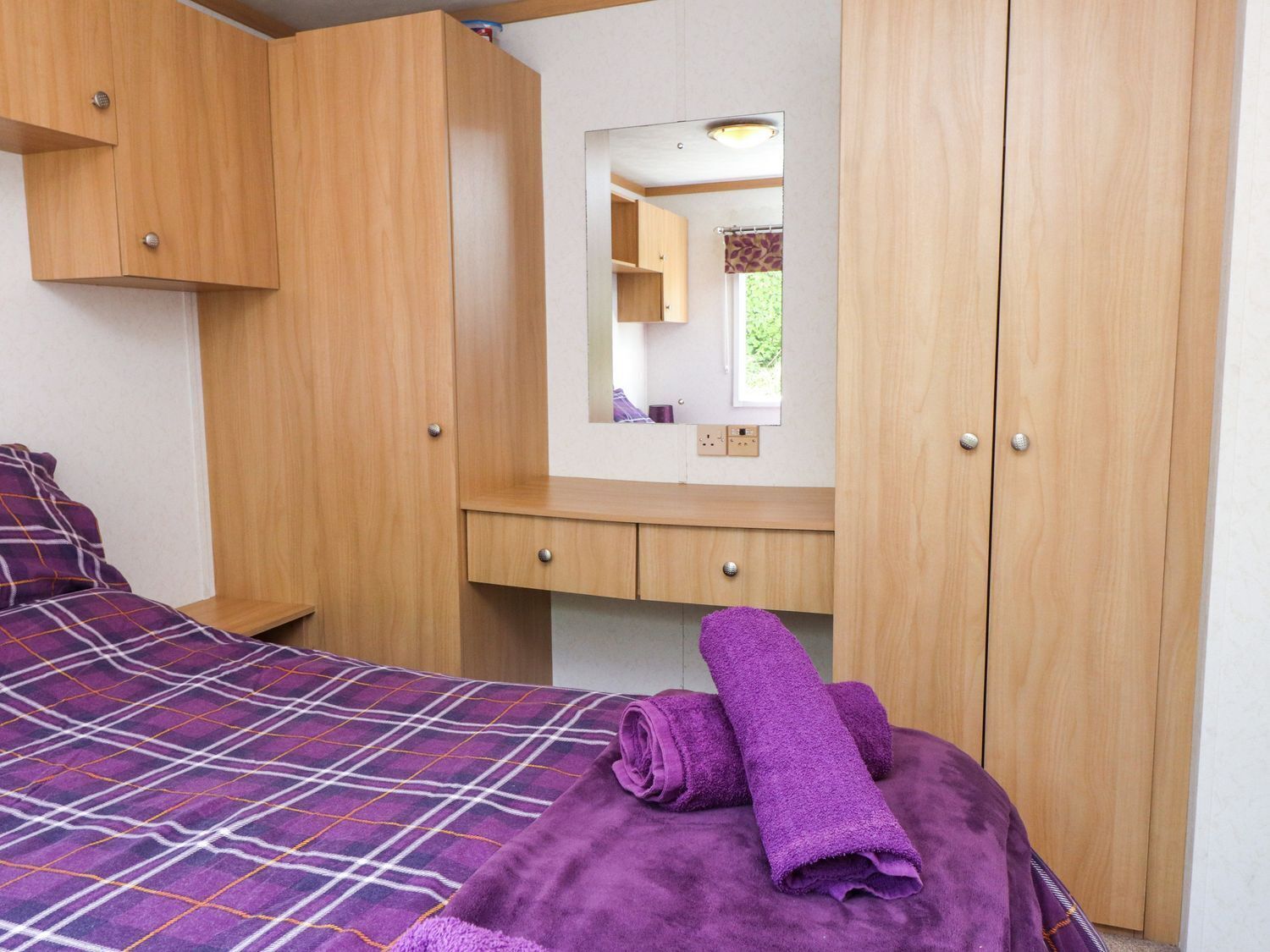 Une chambre à coucher avec un lit, une armoire en bois, un miroir et un petit bureau.