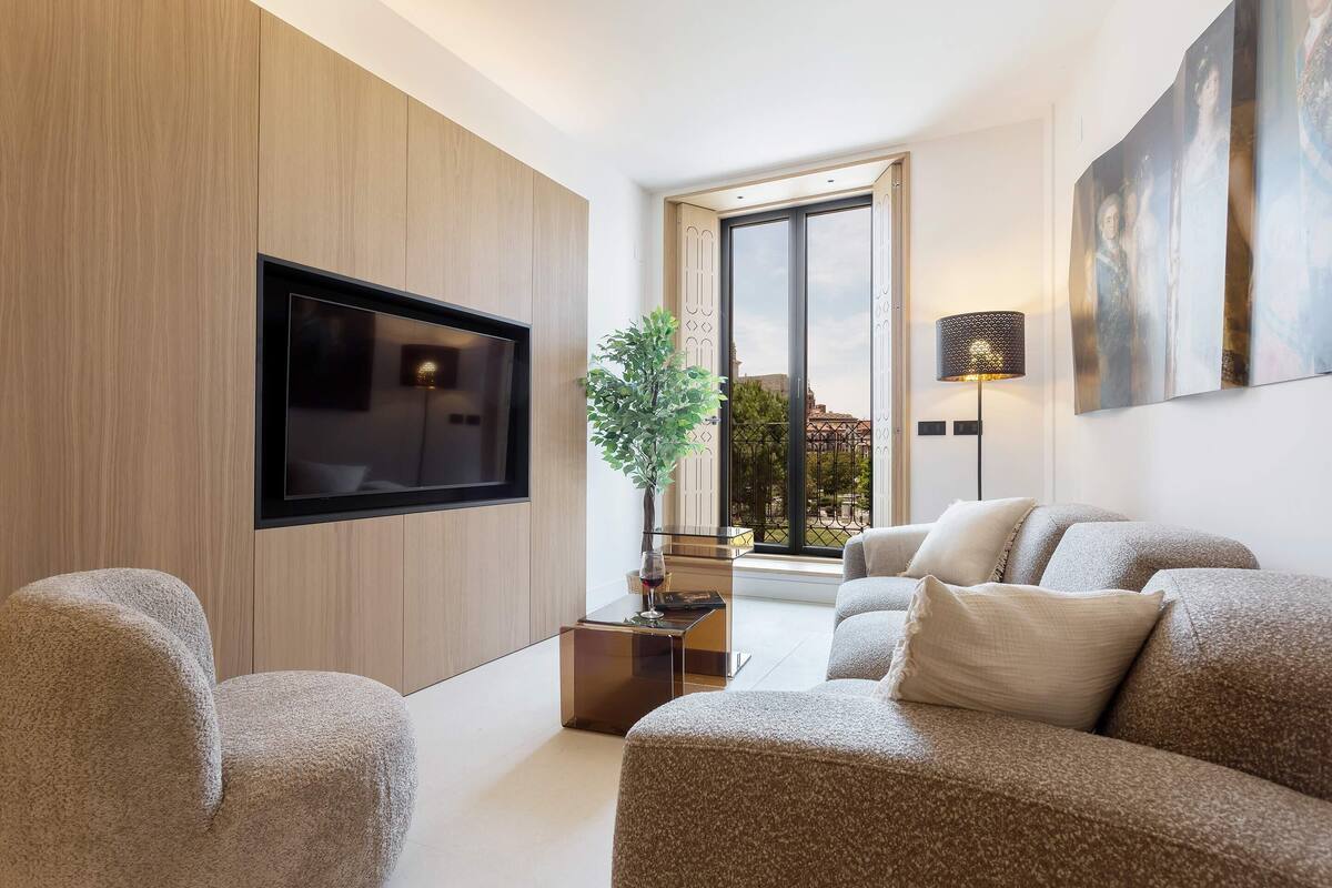Een moderne woonkamer met een flatscreen-tv, een salontafel, een zithoek, een potplant en een groot raam met uitzicht.