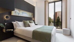 A modern bedroom with a large bed, a bedside table with a plant, a wall-mounted light, and a large window with a view of buildings. -  Genteel Home Solanilla  (Valladolid)