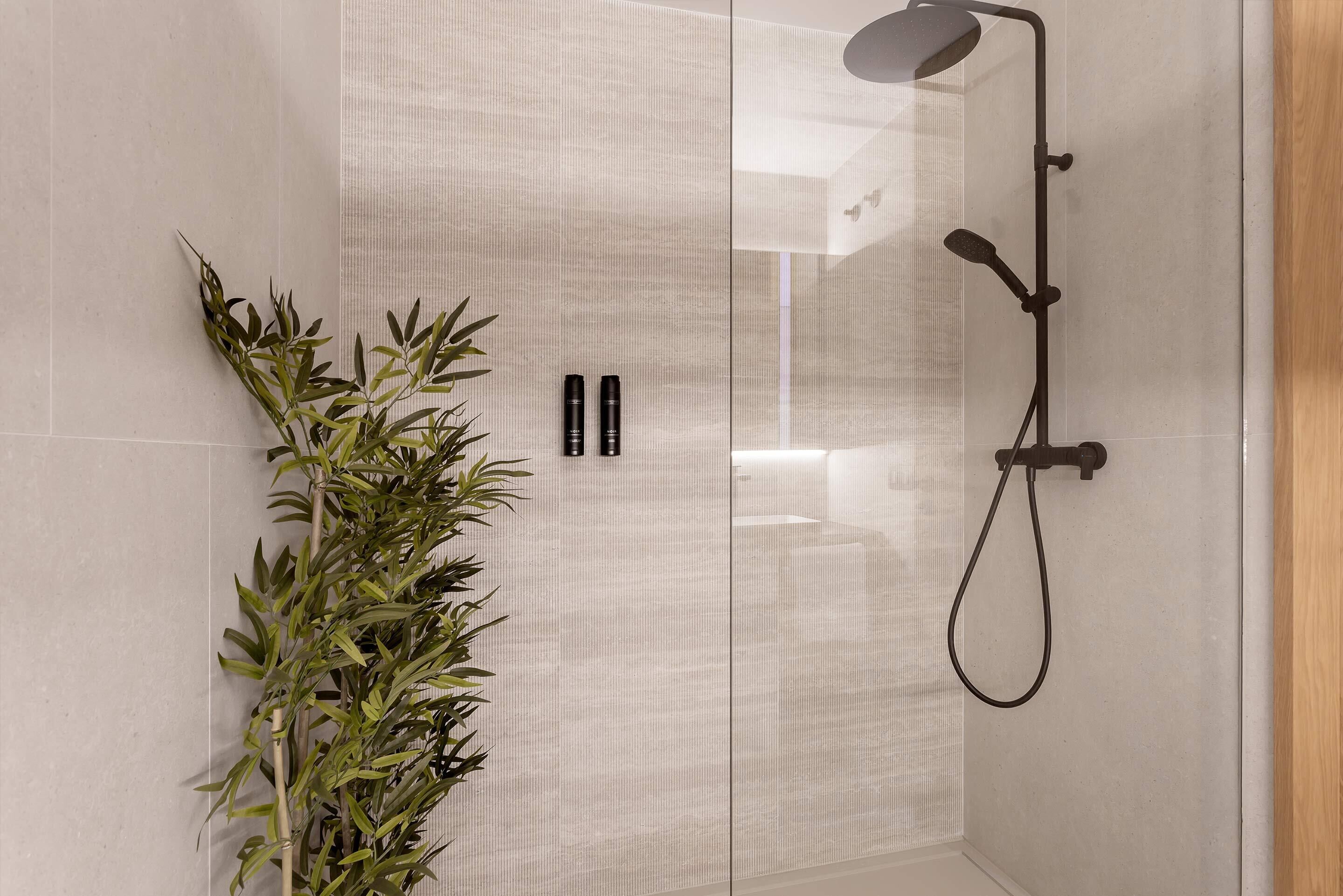 Un baño moderno con cabina de ducha de vidrio, una planta de bambú y dos botellas negras en la pared.