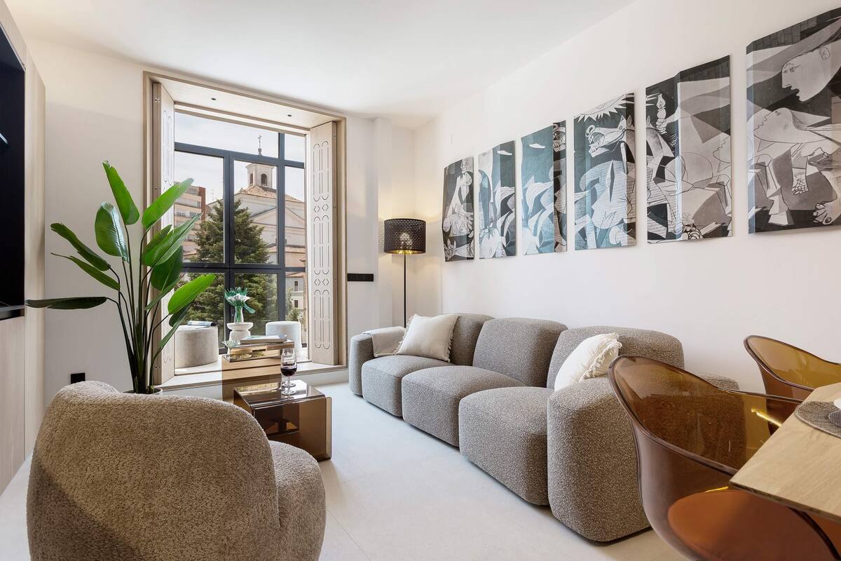 Een moderne woonkamer met een grijze bank, een bijzettafeltje, een plant en abstracte kunst aan de muur.