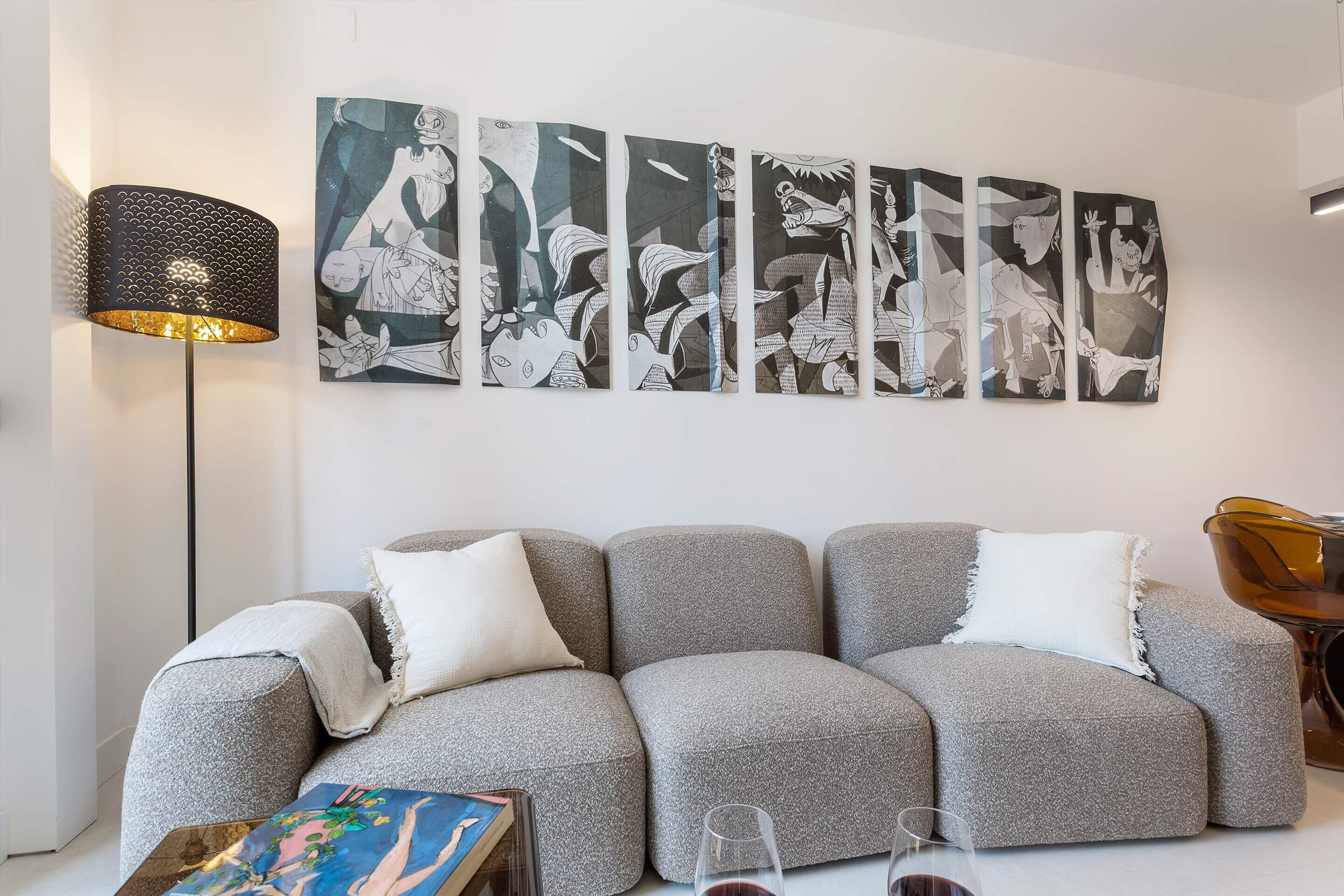 En moderne stue med en grå modulsofa, en gulvlampe og flere abstrakte billeder på væggen.