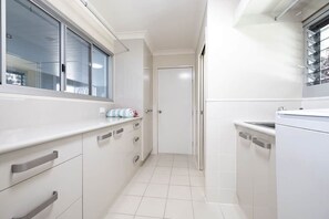 A narrow kitchen with white cabinets, a window, and a door leading to another room.
