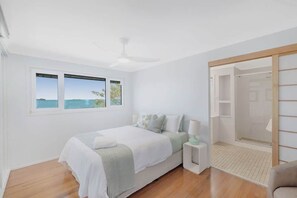 A bedroom with a bed, a nightstand, a ceiling fan, a window with a view, and a walk-in closet.
