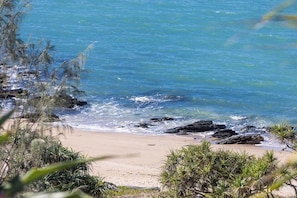 Ein Strand mit klarem Wasser, Felsen und etwas Vegetation.
