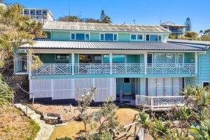Une maison à deux étages dotée d’un balcon, d’un chemin en pierre et d’une végétation tropicale.
