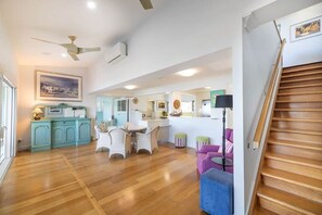 A spacious kitchen with wooden flooring, a dining area with chairs, a staircase, and a ceiling fan.