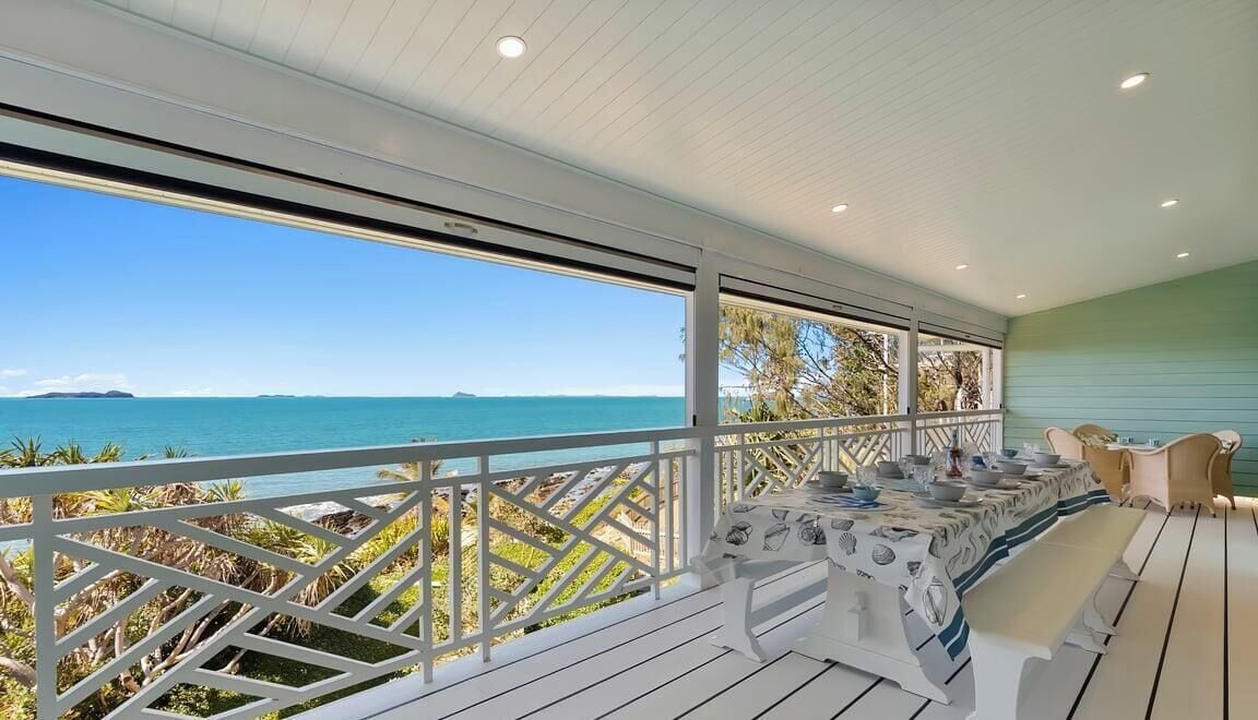 Un espace extérieur abrité, aménagé pour les repas, avec vue sur la mer, des rampes blanches et une table dressée.