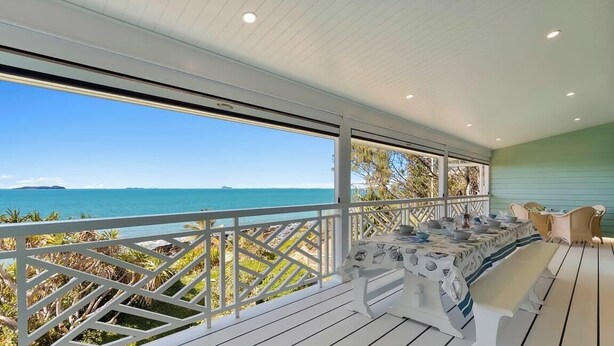 A covered outdoor dining area with a view of the sea, white railings, and a table set for dining. - Silver Waters - Where Your Private Beach Awaits (Zilzie)