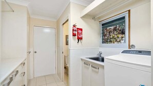 A compact laundry room with a washing machine, a sink, and a fire extinguisher. - Silver Waters - Where Your Private Beach Awaits (Zilzie)
