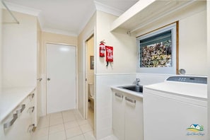 A compact laundry room with a washing machine, a sink, and a fire extinguisher. - Silver Waters - Where Your Private Beach Awaits (Zilzie)