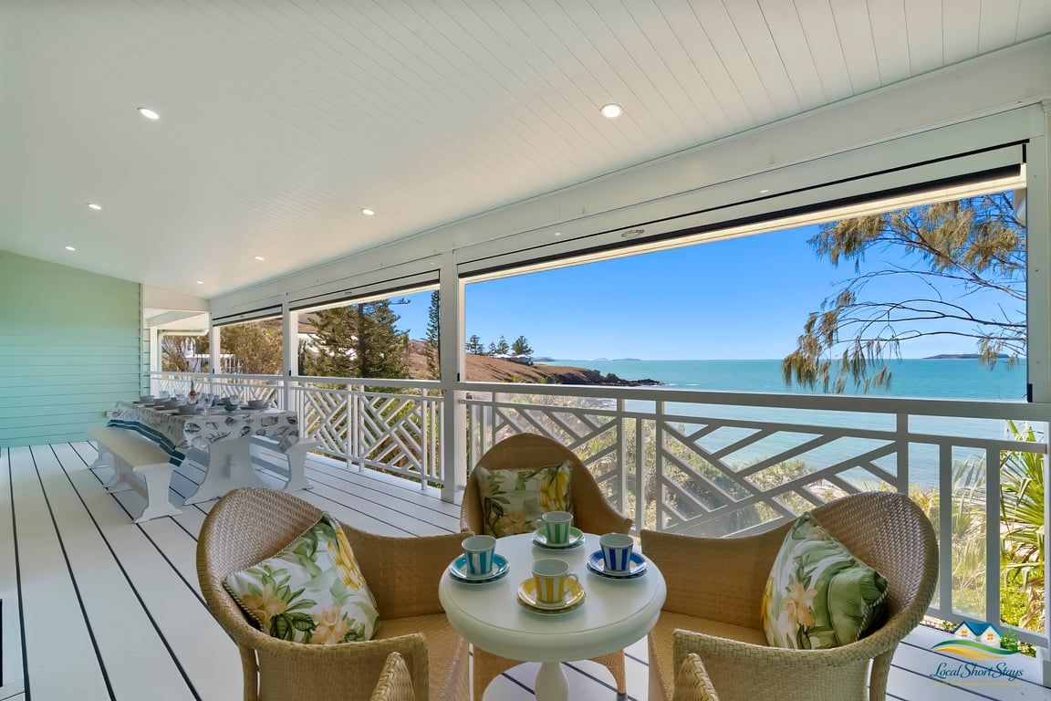 A covered outdoor seating area with a table and chairs, overlooking a scenic view.