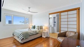 A bedroom with a bed, bedside table, lamp, and a view through a sliding door. - Silver Waters - Where Your Private Beach Awaits (Zilzie)