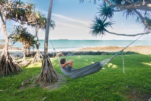 A hammock tied between trees on a grassy area with a beach and ocean in the background.