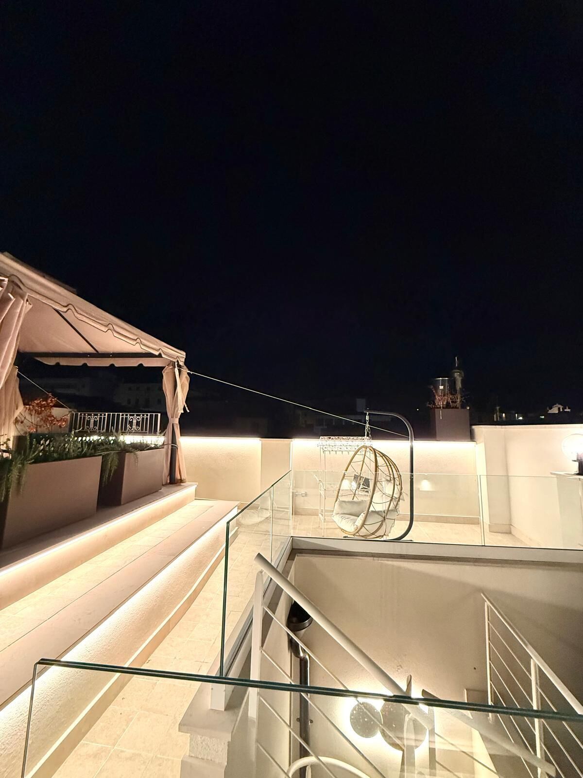 Una terrazza sul tetto con ringhiera in vetro, una poltrona a dondolo e una scala che conduce a un livello superiore.