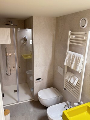A modern bathroom with a glass shower enclosure, a white toilet, a yellow sink, and a towel rack with multiple towels. - Hotel Fiore di Maggio – Boutique Suites in Downtown Matera (Matera)