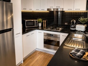 A modern kitchen with stainless steel appliances, a black tiled backsplash, and a black countertop. - 2BR CBD Modern Retreat Pool, Gym & Free Parking (Melbourne)