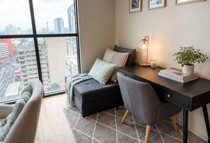 A modern bedroom with a city view, a desk with a lamp, a bookshelf, and a potted plant. - 2BR CBD Modern Retreat Pool, Gym & Free Parking (Melbourne)