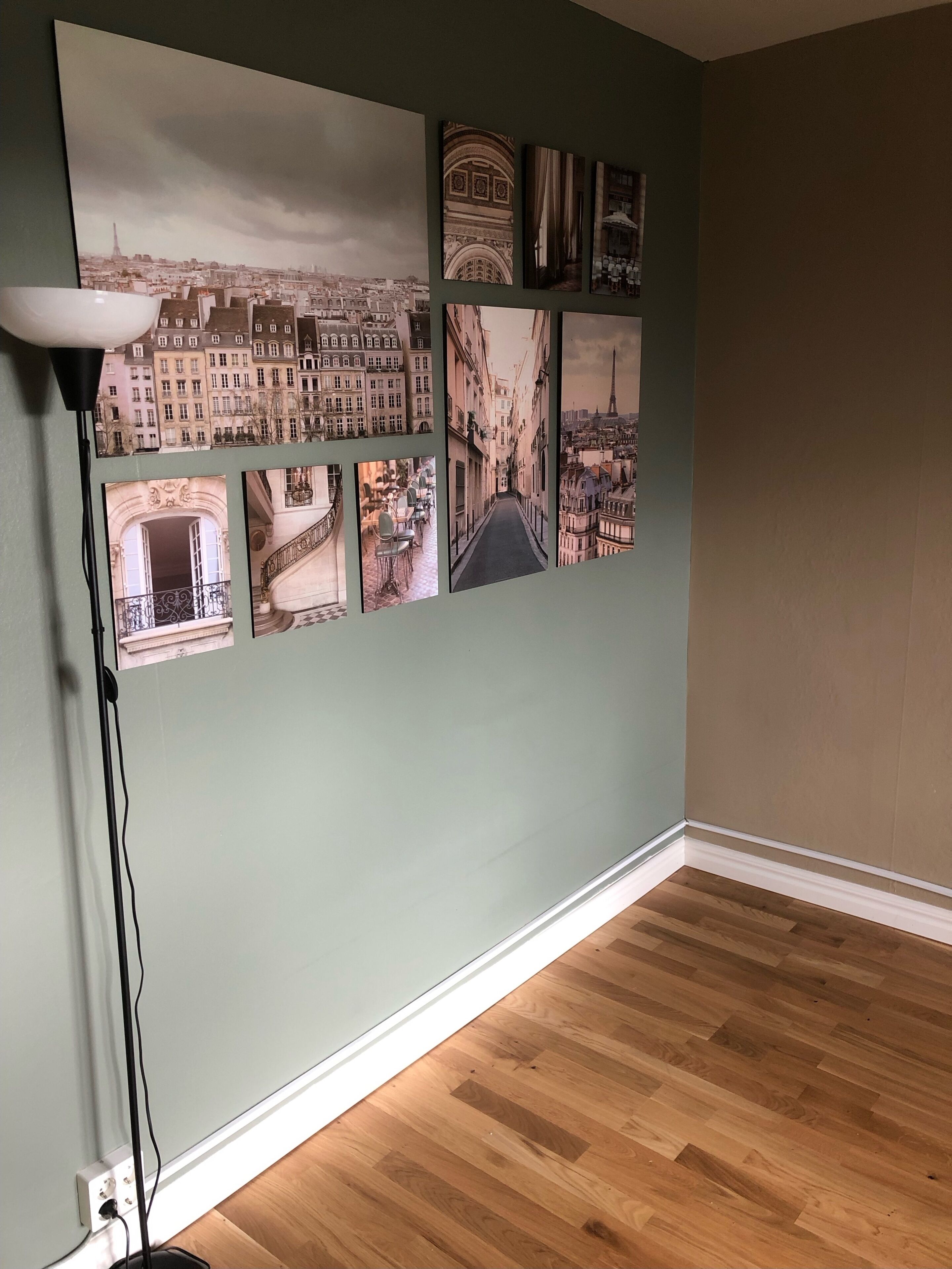 Una stanza con una galleria di fotografie appese al muro, una lampada da terra e un pavimento in legno.