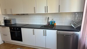 A compact kitchen with white cabinets, a black countertop, a microwave, a dishwasher, and a sink. - Mälartorget - Stay Smart (Västmanlands län)