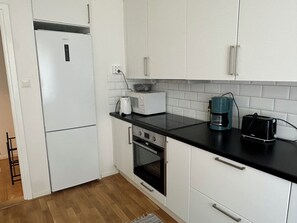 Eine Küche mit weißen Schränken, einer schwarzen Arbeitsplatte, einer Kaffeemaschine, einem Toaster und einem Kühlschrank.