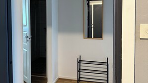 A hallway with a door leading to a dark room, a mirror on the wall, and a metal rack. - Mälartorget - Stay Smart (Västmanlands län)