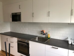 Ett modernt kök med vita skåp, en svart bänkskiva, en inbyggd ugn och en diskho i rostfritt stål.