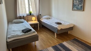 A small, well-lit room with two single beds, a desk, a radiator, and a window with curtains. - Mälartorget - Stay Smart (Västmanlands län)