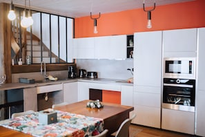 Una cocina moderna con una escalera de madera, electrodomésticos integrados y un comedor con mantel floral.