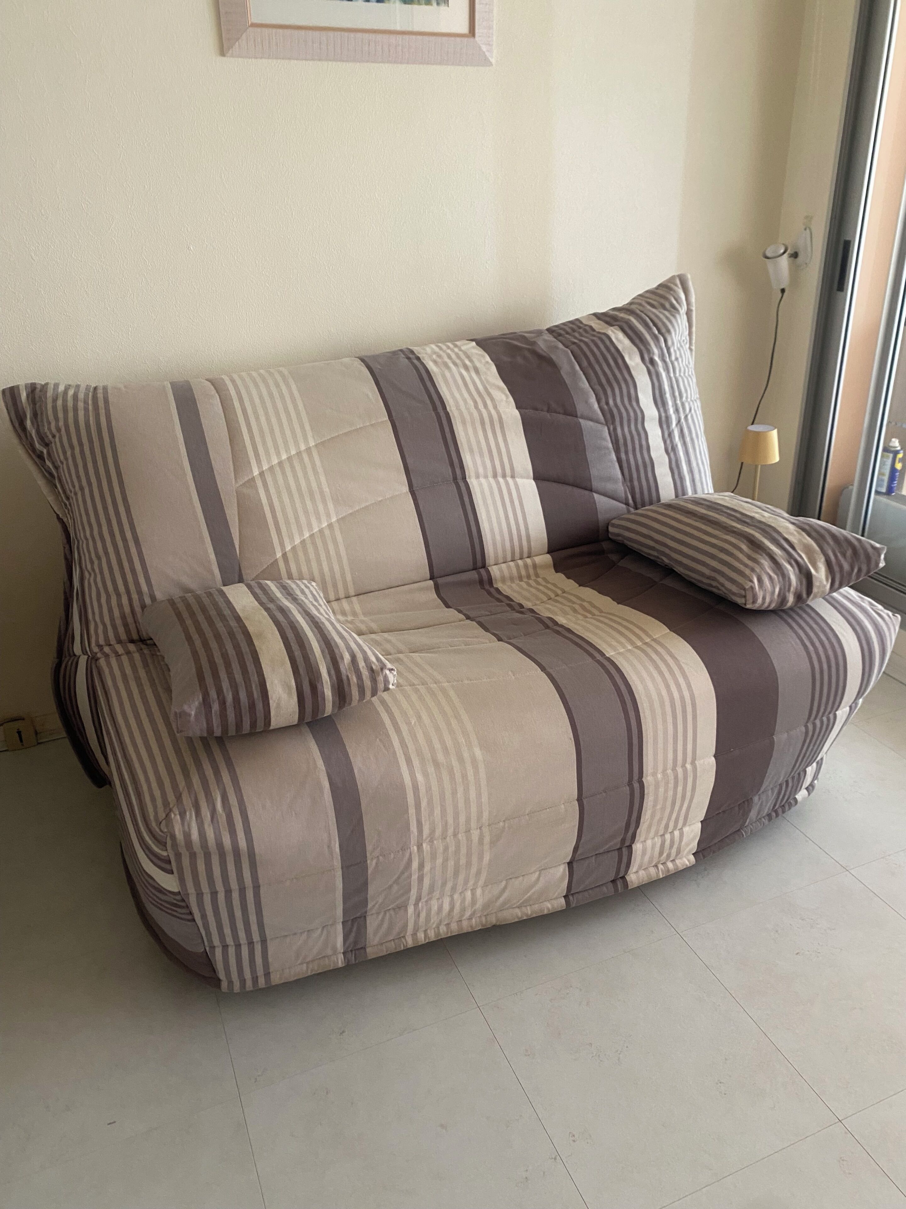 A striped sofa with two cushions, a lamp, and a framed picture on the wall.