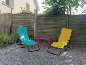 Zwei Gartenlounge-Stühle mit Metallgestellen und Stoffbezügen, ein kleiner rosafarbener Tisch und ein Holzzaun in einer Wohngegend.