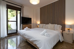 Ein Schlafzimmer mit einem großen Bett, einem Fernseher, einem Nachttisch und Blick durch eine Schiebetür.