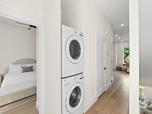 Moderni hotellihuone, jossa on sänky, pesukone ja ovi, joka johtaa parvekkeelle.