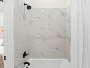 Ein Badezimmer mit einer weißen Badewanne, einer Duschbrause und Marmorwänden.