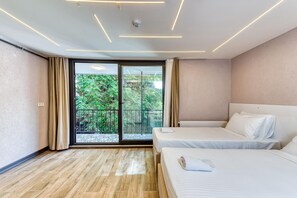 A modern hotel room with two beds, a large sliding glass door to a balcony, and a ceiling with linear lighting.