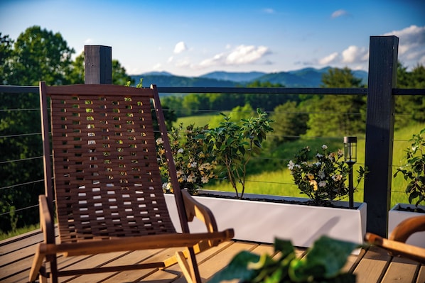 Une terrasse en bois avec une chaise en bois, donnant sur un paysage verdoyant et des montagnes.