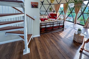 Un vaste espace de vie agrémenté d’un escalier en bois, d’un canapé rouge et offrant une vue sur la verdure grâce à de grandes fenêtres.