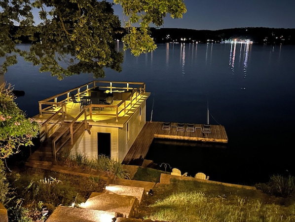 A docked boat with a small deck and a cabin, surrounded by calm water and trees.