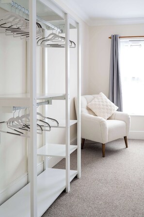 A room with a white closet, a chair with a cushion, and a window with curtains. - 2 Bed Victorian Townhouse with Parking & Courtyard (Impington)