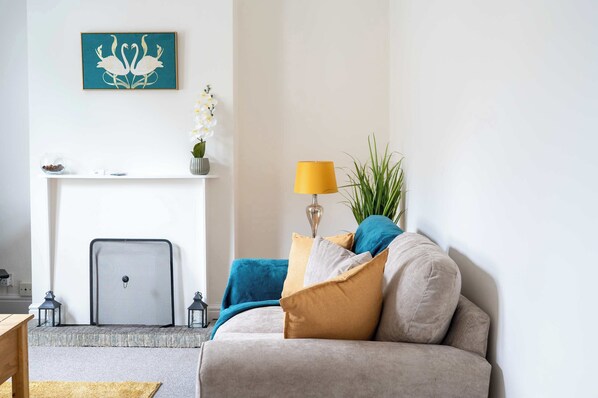 A living room with a sofa, a lamp, a fireplace, and a wall-mounted artwork. - 2 Bed Victorian Townhouse with Parking & Courtyard (Impington)