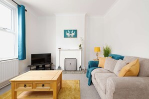 A living room with a sofa, coffee table, TV, fireplace, and artwork on the wall. - 2 Bed Victorian Townhouse with Parking & Courtyard (Impington)