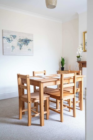 A wooden dining table with chairs, a world map on the wall, a plant, and a mirror. - 2 Bed Victorian Townhouse with Parking & Courtyard (Impington)