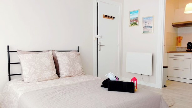 A bedroom with a bed, a bedside table with a lamp, a door, and a wall-mounted radiator. - A Cozy Retreat in the Heart of Boulogne-sur-Mer (Boulogne-sur-Mer)