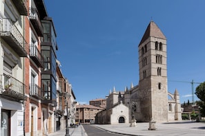 A historic building with a prominent tower, a street with multi-story buildings, and a clear blue sky. - Exclusive Apartment in Valladolid Solanilla I (Valladolid)