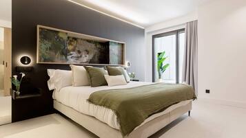 Un dormitorio moderno con una cama grande, una obra de arte colgada en la pared, una mesita de noche y una ventana con cortinas.