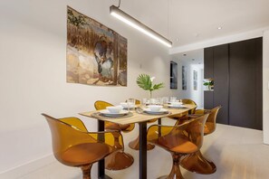 A modern dining area with a table set for six, surrounded by orange chairs, a large painting on the wall, and a plant on the table. - Exclusive Apartment in Valladolid Solanilla I (Valladolid)