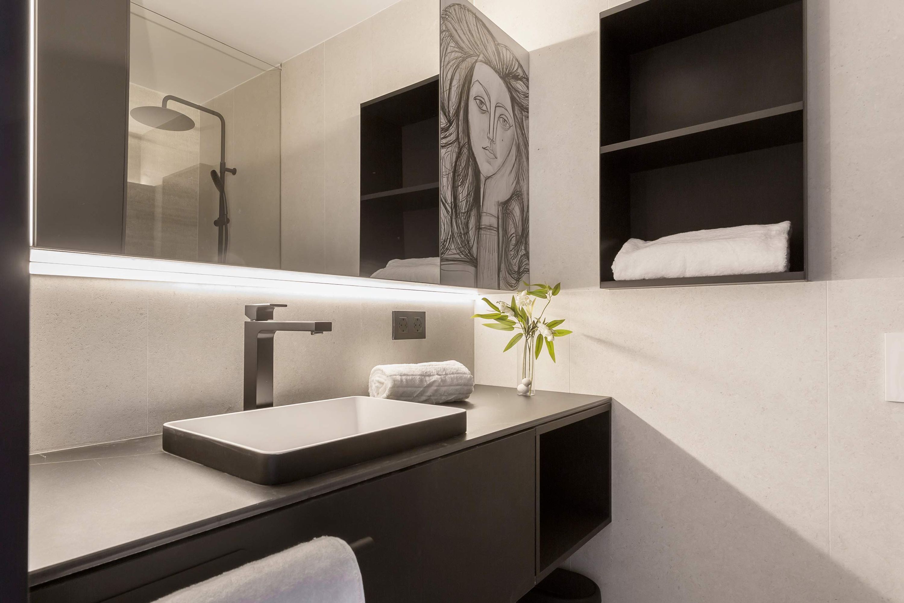 Un baño moderno con un espejo grande, un lavamanos rectangular, una toalla y un florero con una planta.