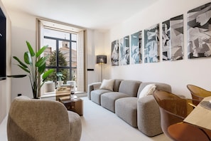 A modern living room with a sofa, armchairs, a coffee table, and a floor lamp. There are abstract paintings on the wall and a large window with a view of buildings. - Bright Apartment in the Heart of Valladolid Solanilla IV (Valladolid)